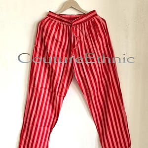 May include: Red and pink striped pajama pants hanging on a wooden hanger. The pants have a drawstring waist and white trim at the hem. The text "Couture Ethnic" is visible on the pants.