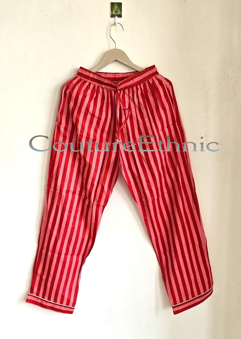 May include: Red and pink striped pajama pants hanging on a wooden hanger. The pants have a drawstring waist and white trim at the hem. The text "Couture Ethnic" is visible on the pants.
