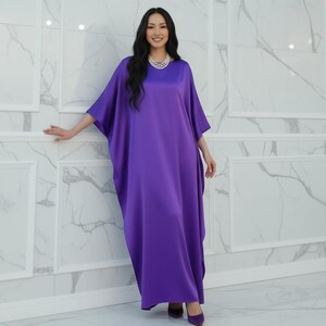 May include: A long, flowing, purple dress with wide sleeves. The dress is made of a smooth, shiny fabric and is worn with matching purple shoes. A pearl necklace is also worn.