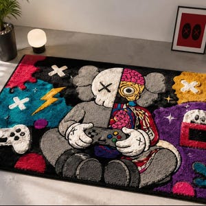 Puede incluir: Una alfombra rectangular con un personaje de dise&ntilde;o dividido que sostiene un mando de videojuegos. El personaje es mitad gris y mitad anat&oacute;mico con detalles de cerebro y esqueleto. El fondo incluye formas vibrantes en azul, amarillo y morado.