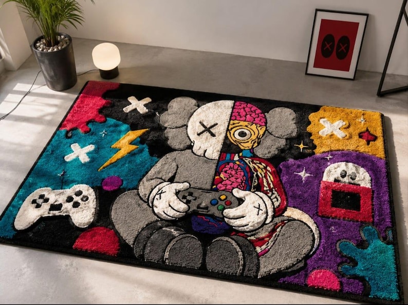 Puede incluir: Una alfombra rectangular con un personaje de dise&ntilde;o dividido que sostiene un mando de videojuegos. El personaje es mitad gris y mitad anat&oacute;mico con detalles de cerebro y esqueleto. El fondo incluye formas vibrantes en azul, amarillo y morado.