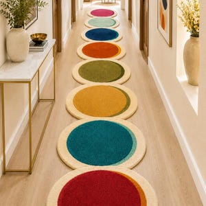 May include: A long runner rug featuring a series of circular shapes in various colours including red, teal, yellow, olive green, orange, blue, light blue, and magenta, each with a cream-coloured border, arranged in a straight line on a wooden floor.