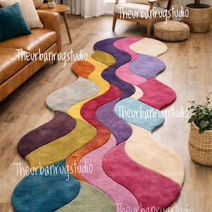 May include: A multi-coloured, wave-shaped rug. The rug has a distinctive design with shades of purple, pink, yellow, and blue. It is placed on a wooden floor in a living room setting.