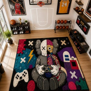 Puede incluir: Una alfombra rectangular que presenta un personaje de dise&ntilde;o dividido sosteniendo un mando de videojuegos. El personaje es mitad gris y mitad anat&oacute;mico, mostrando &oacute;rganos internos. La alfombra incluye elementos gr&aacute;ficos coloridos.
