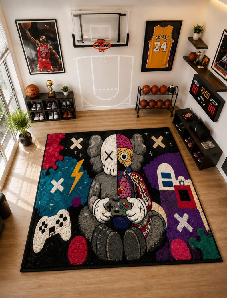 Puede incluir: Una alfombra rectangular que presenta un personaje de dise&ntilde;o dividido sosteniendo un mando de videojuegos. El personaje es mitad gris y mitad anat&oacute;mico, mostrando &oacute;rganos internos. La alfombra incluye elementos gr&aacute;ficos coloridos.