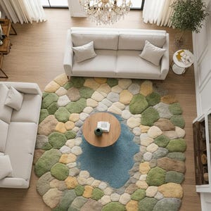 May include: Overhead view of a living room with a large, round rug resembling a pond with colorful stones. The rug is surrounded by two white sofas, a wooden coffee table, and a crystal chandelier. The room has large windows and hardwood floors.