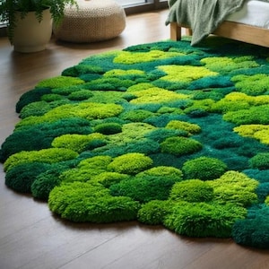 May include: A round rug with a textured, moss-like appearance. The rug features varying shades of green, creating a natural, organic look. The rug is placed on a wooden floor, and the design resembles a landscape.