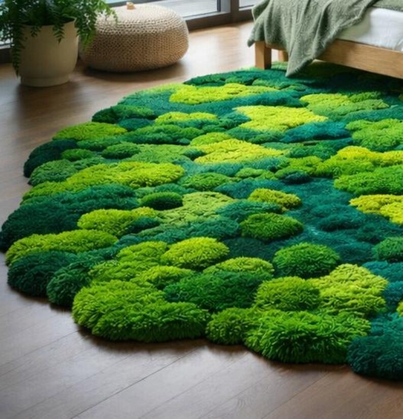 May include: A round rug with a textured, moss-like appearance. The rug features varying shades of green, creating a natural, organic look. The rug is placed on a wooden floor, and the design resembles a landscape.
