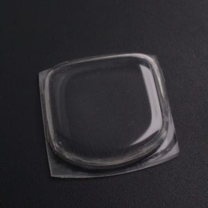 May include: A clear, square-shaped plastic item with rounded corners. The item appears to be a protective cover or a component of a larger product. The plastic is transparent, allowing a view of the surface beneath.