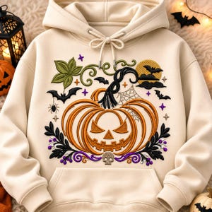 May include: A cream-colored hooded sweatshirt featuring an embroidered design of a central orange jack-o'-lantern, a small skull, black bats, a spider web, green leaves, and purple accents. The hoodie includes a front kangaroo pocket and drawstrings.
