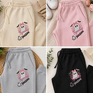 May include: Four pairs of sweatpants in cream, light pink, heather gray, and black. Each pair features an embroidered graphic of a ghost with a pink bow, a spiderweb, bats, and the text Spooky season in black and pink script lettering.