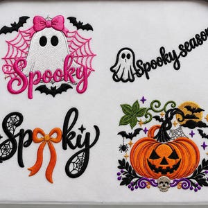May include: An embroidery hoop containing four Halloween designs on white fabric: a white ghost with a pink bow and web, the word Spooky in pink, a small ghost with the text Spooky season, the word Spooky in black with an orange bow, and a jack-o'-lantern.
