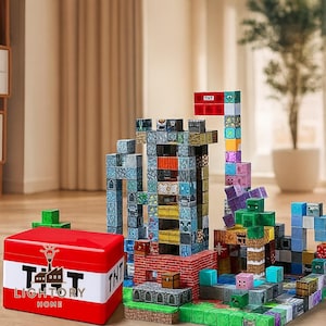 Puede incluir: Un colorido juego de bloques de construcción con una caja de almacenamiento roja y blanca. Los bloques están dispuestos para parecerse a un paisaje urbano con varias estructuras, incluyendo una torre y un edificio con un letrero de TNT. La caja tiene el texto "LIGHTORY HOME".