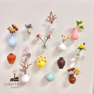 Puede incluir: Una colección de pequeños y coloridos jarrones, cada uno con un tipo diferente de flor o planta seca. Los jarrones son de varias formas y colores, incluyendo azul, rosa, amarillo y marrón. La imagen incluye el texto "LIGHTORY HOME".