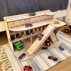 Op de afbeelding: Een houten speelgoed autogarage en hellingbaan set met meerdere speelgoedauto's. De garage heeft genummerde vakken en een hellingbaan. De set is gemaakt van lichtgekleurd hout en is ontworpen voor kinderspel.