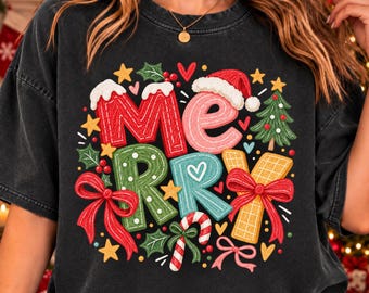 May include: A black short-sleeve t-shirt featuring a colorful graphic print that spells out the word MERRY. The letters are decorated with holiday elements including a Santa hat, red bows, a candy cane, a small Christmas tree, and stars.