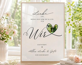 May include: A rectangular framed print with white background and black text reading: Liebe ist, wenn aus dem Du & Ich ein Wir entsteht. Alles Liebe & Gute zur Hochzeit! A heart-shaped cutout reveals a 100 Euro banknote inside the word Wir.