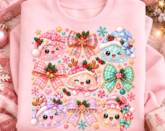 May include: A light pink sweatshirt featuring a graphic print of various smiling, winking characters wearing winter hats, surrounded by colorful plaid bows, holly berries, candy canes, and small gold stars on a soft pastel background.
