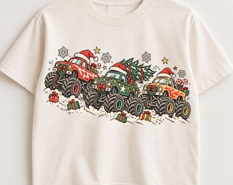 May include: A cream-colored short-sleeve t-shirt featuring a graphic of three monster trucks wearing Santa hats. The trucks are decorated with Christmas wreaths, carrying gifts and a pine tree, surrounded by snowflakes and stars.