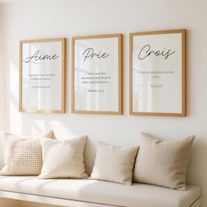 Peut inclure: Trois impressions d'art encadrées avec des citations inspirantes en français. Les impressions sont dans des cadres en bois avec des fonds blancs et du texte noir. Les citations sont "Aime", "Prie" et "Crois". Des coussins beiges et un banc sont au premier plan.