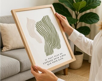 May include: Framed art print featuring abstract shapes in beige and olive green. The artwork includes the French text "IL FAUT PLUS DE COURAGE POUR AIMER QUE POUR HAÏR" in black font, set within a natural wood frame.