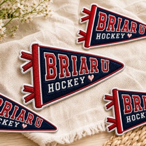 May include: Navy blue and red pennant patches with the text "BRIAR U HOCKEY" in white and red. Each patch has a red border and decorative red ribbons. A small pink heart is included in the design.