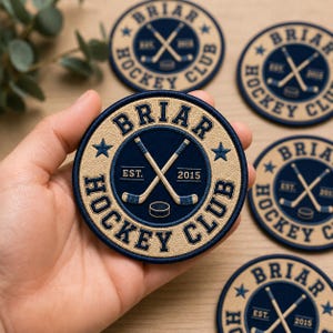 May include: Circular embroidered patch with the text "BRIAR HOCKEY CLUB" in navy blue and tan. The patch features crossed hockey sticks, a hockey puck, and the year "2015". Several patches are visible.