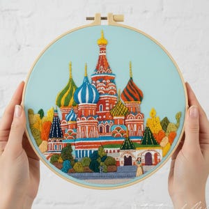 May include: An embroidered hoop art piece featuring a colorful depiction of St. Basil's Cathedral in Moscow. The artwork showcases the iconic onion domes in shades of red, blue, green, and gold, set against a light blue background.
