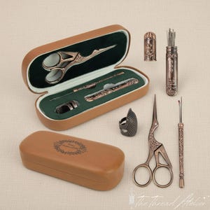 Puede incluir: Un kit de costura con herramientas de color bronce, que incluye tijeras, agujas y un dedal, presentado en un estuche marrón con interior verde. Incluye un abridor de costuras y un protector de dedos. Para costura y manualidades.