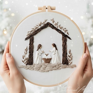 Puede incluir: Arte de aro bordado con una escena de la Natividad. Dos figuras con vestidos blancos están de pie bajo una estructura marrón, con una cesta de flores entre ellas. El bordado está sobre un fondo blanco, enmarcado por un aro de madera.