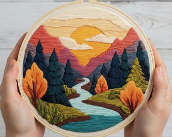 May include: A hand-stitched embroidery hoop featuring a landscape scene. The design includes a sunset with a yellow sun, mountains, trees, and a river. The color palette includes shades of orange, yellow, green, and blue. The embroidery is set in a wooden hoop.