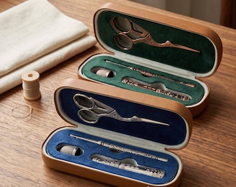 Könnte beinhalten: Zwei ovale hellbraune Etuis mit Nähwerkzeug. Das obere Etui hat ein dunkelgrünes Innenfutter mit kupferfarbener Schere, Fingerhut und Nadelwerkzeug. Das untere Etui hat ein blaues Innenfutter mit silberfarbener Schere, Fingerhut und Nadelwerkzeug.