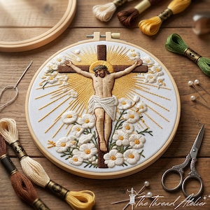 Può includere: Opera d'arte ricamata di Gesù sulla croce, circondata da un'aureola e fiori bianchi. Il ricamo è posto in un telaio di legno, con rocchetti di filo e strumenti per ricamo. Il logo The Thread Atelier è visibile.
