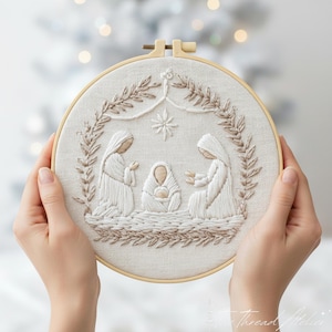 Könnte beinhalten: Gestickte Weihnachtsszene in einem runden Holzrahmen. Das Kunstwerk zeigt die Geburt Christi mit Maria, Josef und dem Jesuskind, umgeben von einem Kranz. Die Stickerei ist in Weiß- und Beigetönen gehalten und erzeugt einen strukturierten, dreidimensionalen Effekt.