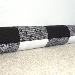 May include: Black and white checkered doorstop. The doorstop is a cylinder shape and is made of fabric.