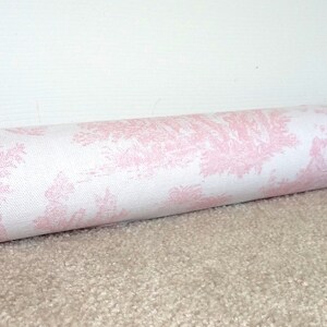 May include: A white doorstop with a pink floral pattern. The doorstop is rolled up and lying on a beige carpet.