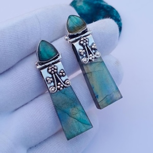 May include: A pair of drop earrings featuring elongated rectangular labradorite stones with blue and green iridescence. Each earring has a triangular labradorite top piece set in silver, connected by a decorative silver metal section with floral motifs.