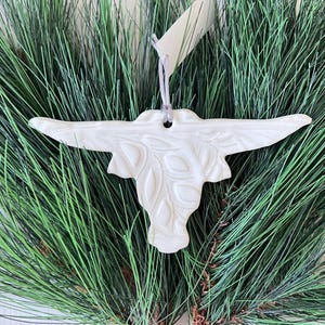 May include: White ceramic ornament shaped like a longhorn steer head with a detailed embossed design. The ornament has a loop for hanging.