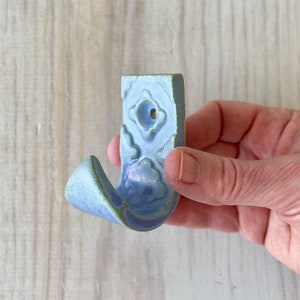 May include: A light blue ceramic hook with a decorative floral pattern. The hook has a hole for hanging on a wall.