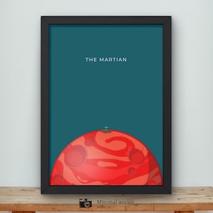 May include: Framed art print featuring a stylized illustration of a red planet with a small sprout, set against a teal background. The text "THE MARTIAN" is displayed in white. The artwork is in a black frame.