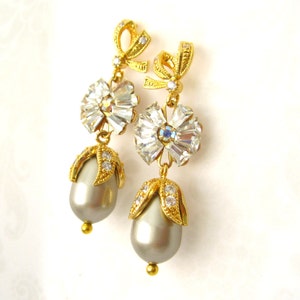May include: A pair of gold tone dangle earrings with a pearl drop and crystal accents. The earrings feature a bow design at the top and a flower-shaped crystal cluster in the middle.