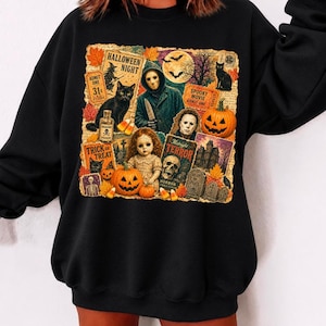 以下が含まれることがあります： 黒の長袖スウェットシャツ。ハロウィーンをテーマにしたカラフルなグラフィックプリントが大きく施されており、仮面をつけた人物、人形、ジャック・オー・ランタン、黒猫、墓石、文字が書かれたヴィンテージ風の映画チケットなどが描かれています。