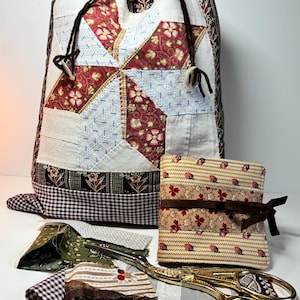 May include: A patchwork drawstring bag with a starburst design in red, white, and blue. A matching needle case and fabric scraps are next to gold scissors. A collection of sewing and quilting supplies.