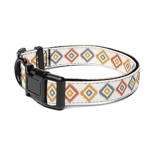 Puede incluir: Collar para perros con fondo crema y un patrón repetido de diamantes naranjas, amarillos y azules. Tiene una hebilla de plástico negro y una anilla en D de metal negro. Accesorio para mascotas.