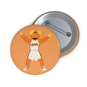 May include: Orange button featuring a cartoon mascot in a basketball uniform with the word "SUN" on the jersey. The mascot has its arms raised. A second button is visible in the background.