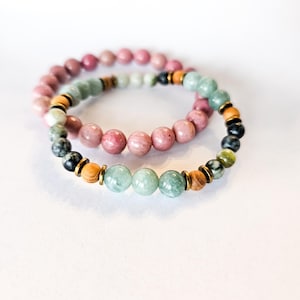 Può includere: Due braccialetti elastici con perline rotonde. Un braccialetto è composto da perline di rodonite rosa. Il secondo presenta un mix di perline in legno verde chiaro, verde scuro e beige, arricchite da piccoli anelli distanziatori dorati.