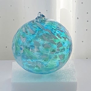 May include: A blue, green, and white glass ornament with a swirl pattern. The ornament is round and has a shiny finish.