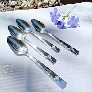 May include: Four silver spoons with an ornate design on the handle. The spoons are arranged in a row on a white surface.