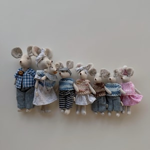 May include: A collection of handmade mouse dolls dressed in miniature clothing. The mice wear outfits including blue plaid shirts, striped sweaters, and floral dresses. Each doll has large, floppy ears and is posed upright.