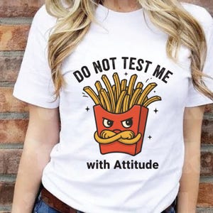 K&ouml;nnte beinhalten: Wei&szlig;es T-Shirt mit einem Cartoon-Design von Pommes Frites in einer roten Schachtel mit einem w&uuml;tenden Gesicht und einem Schnurrbart. Der Text &uuml;ber den Pommes lautet "DO NOT TEST ME" und darunter "with Attitude".